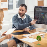 Perfect_presentation._Lively_young_man_pointing_at_the_computer_screen_and_presenting_his_project_to_his_female_boss_while_the_woman_listening_to_him_attentively