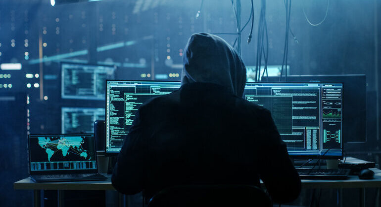 Dangerous_Hooded_Hacker_Breaks_into_Government_Data_Servers_and_Infects_Their_System_with_a__Virus._His_Hideout_Place_has_Dark_Atmosphere,_Multiple_Displays,_Cables_Everywhere.