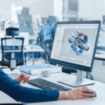 Industrial_female_Engineer_Working_on_a_Personal_Computer,_Screen_Shows_CAD_Software_with_3D_Prototype_of_Engine._Busy_Factory_with_Professional_Workers_High-Tech_Machinery