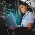 Laptop,_network_and_data_center_with_a_black_woman_it_support_engineer_working_in_a_dark_server_room._Computer,_cybersecurity_and_analytics_with_a_female_programmer_problem_solving_or_troubleshooting.
