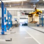 Flying_delivery_drone_transferring_parcel_box_from_distribution_warehouse_to_automotive_garage_customer_service_repair_center_background._Modern_innovative_technology_and_gadget_concept._