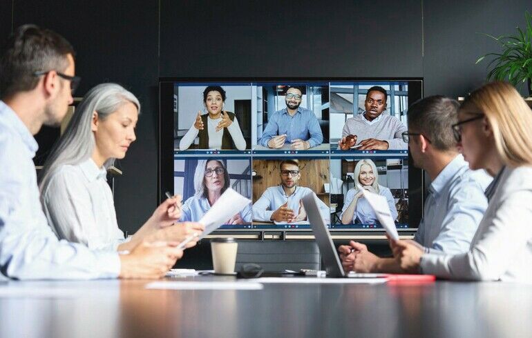 Global_corporation_online_videoconference_in_meeting_room_with_diverse_people_sitting_in_modern_office_and_multicultural_multiethnic_colleagues_on_big_screen_monitor._Business_technologies_concept.