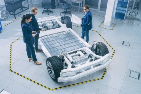 Automotive_Design_Engineers_Talking_while_Working_on_Electric_Car_Chassis_Prototype._In_Innovation_Laboratory_Facility_Concept_Vehicle_Frame_Includes_Wheels,_Suspension,_Engine_and_Battery.