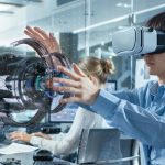 Computer_Science_Engineer_wearing_Virtual_Reality_Headset_Works_with_3D_Model_Hologram_Visualization,_Makes_Gestures._In_the_Background_Engineering_Bureau_with_Busy_Coworkers.