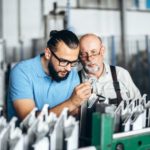 Young_manager_with_beard_showing_and_inspecting_working_process_of_adult_professional_worker_on_the_big_factory