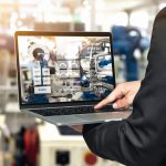 Engineer_hand_using_laptop_with_machine_real_time_monitoring_system_software._Blur_automation_robot_arm_machine_in_smart_factory_Industry_4th_iot_,_digital_manufacturing_operation_technology_concept.